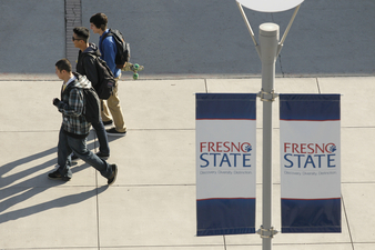 Three students walking under the Fresno State banner.