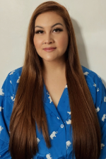Woman in a blue shirt patterned with white elephants stands in front of a beige wall.