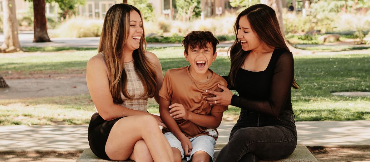 photo of two parents sitting on a bench with their child in between them and they are laughing and smiling together 