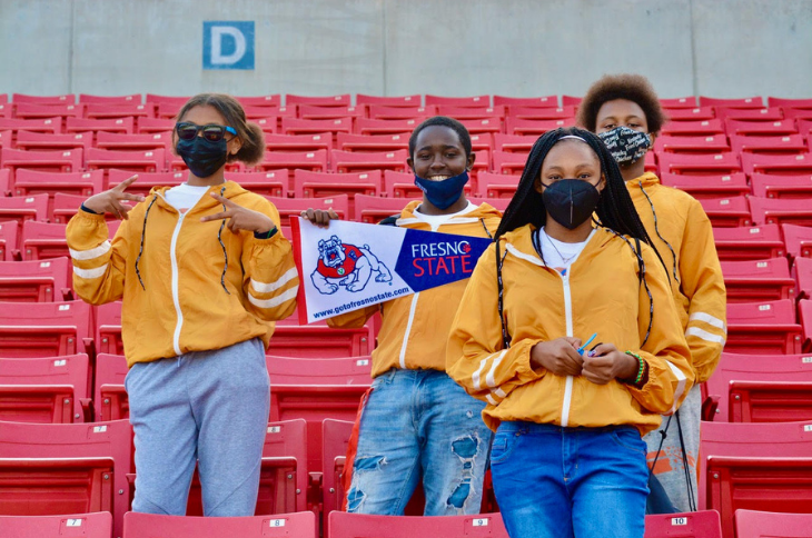 four students in yellow jackets standing in stadium of red seats