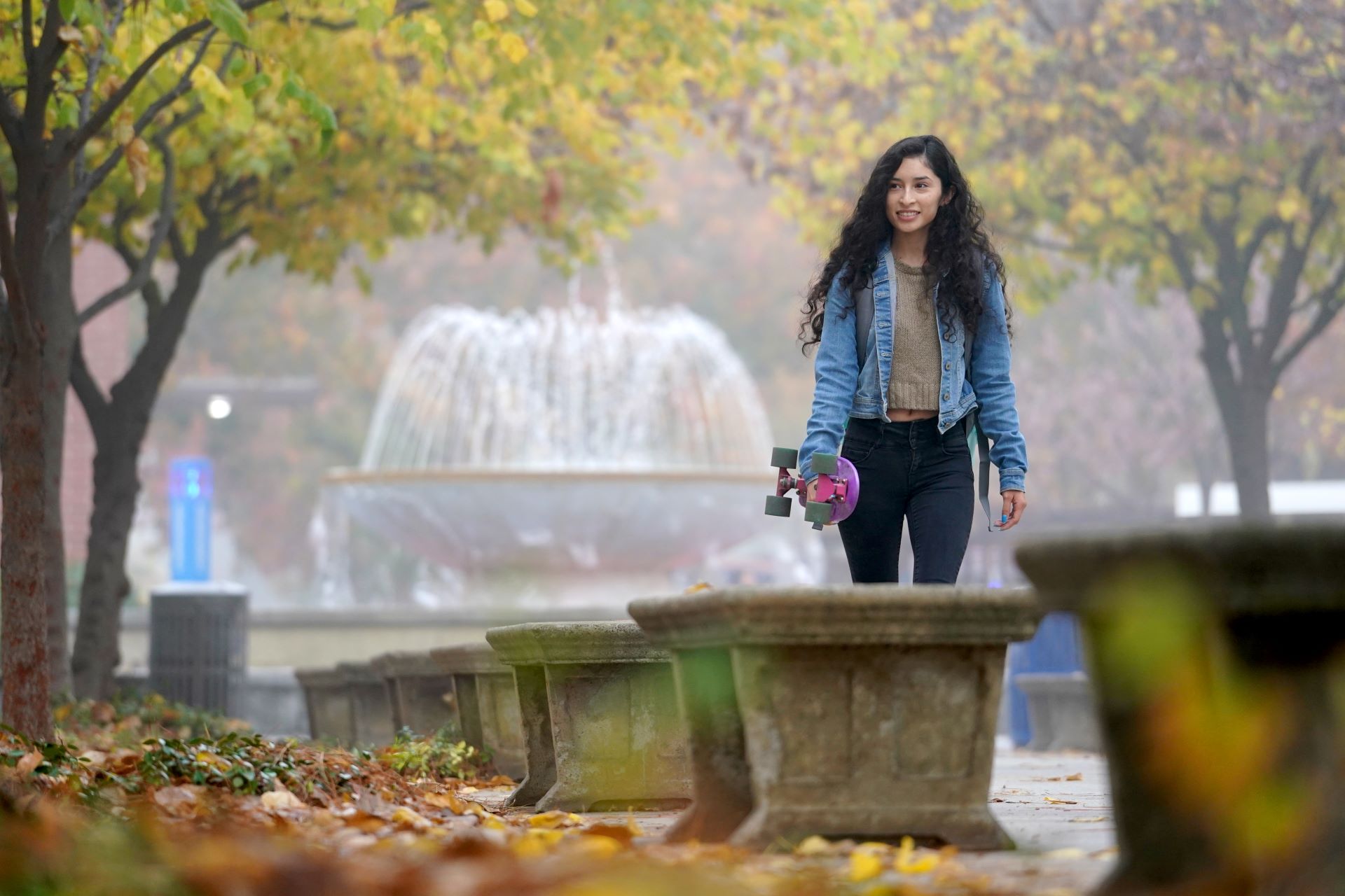 student walking by fountain holding skateboard