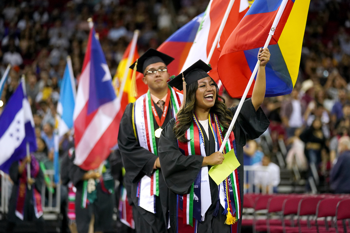 Graduates walking into ceremony carrying Latin American countries' flags