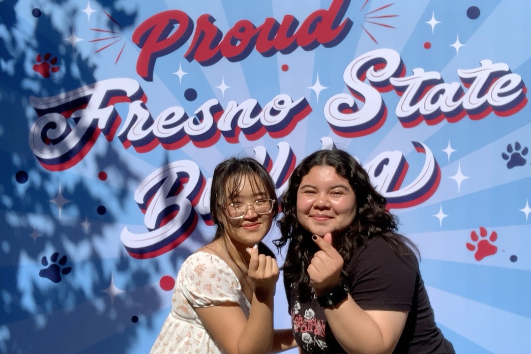 Two female students pose in front of a Fresno State backdrop