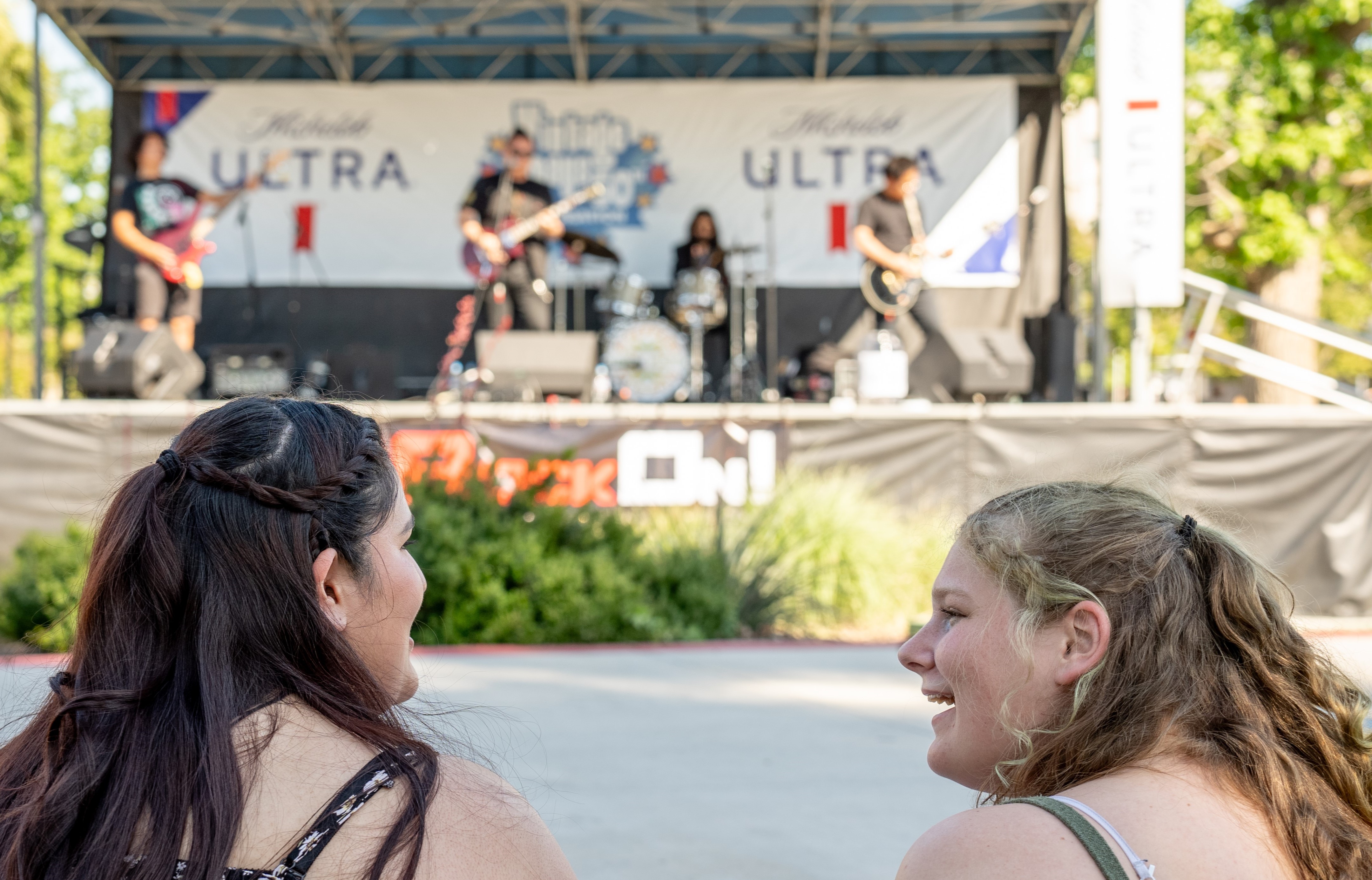 Two students sit on the lawn, enjoying the band performing