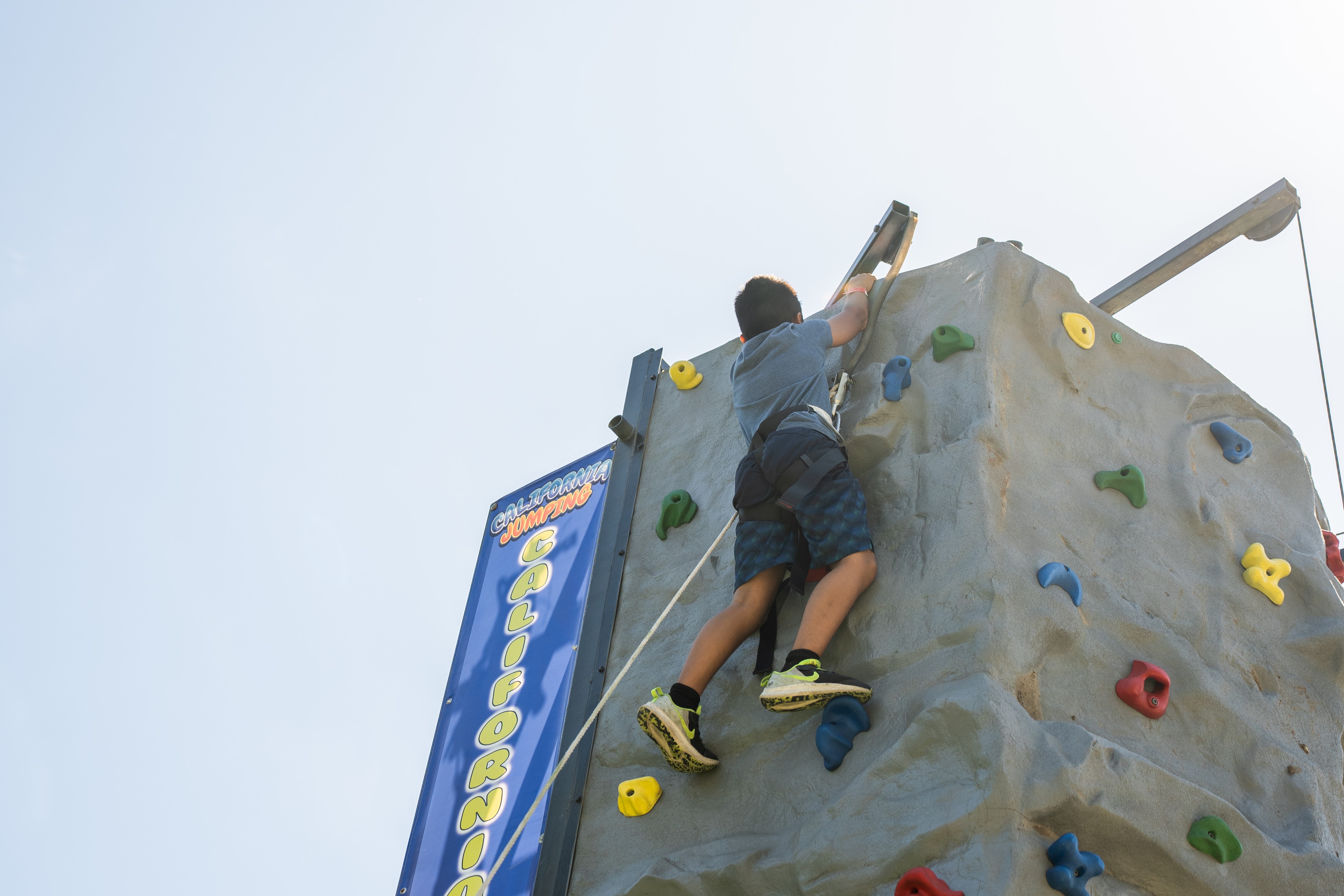 A boy reaches the top of the rock climbing wall and rings the bell victoriously