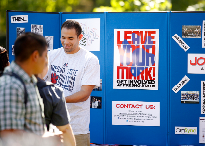 Student in front of a display board chatting with another student while tabling.