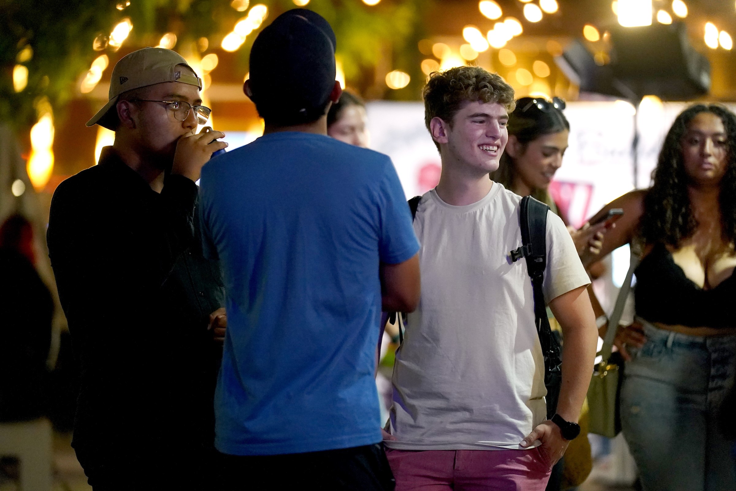 Three male students enjoy the night, standing under twinkling lights