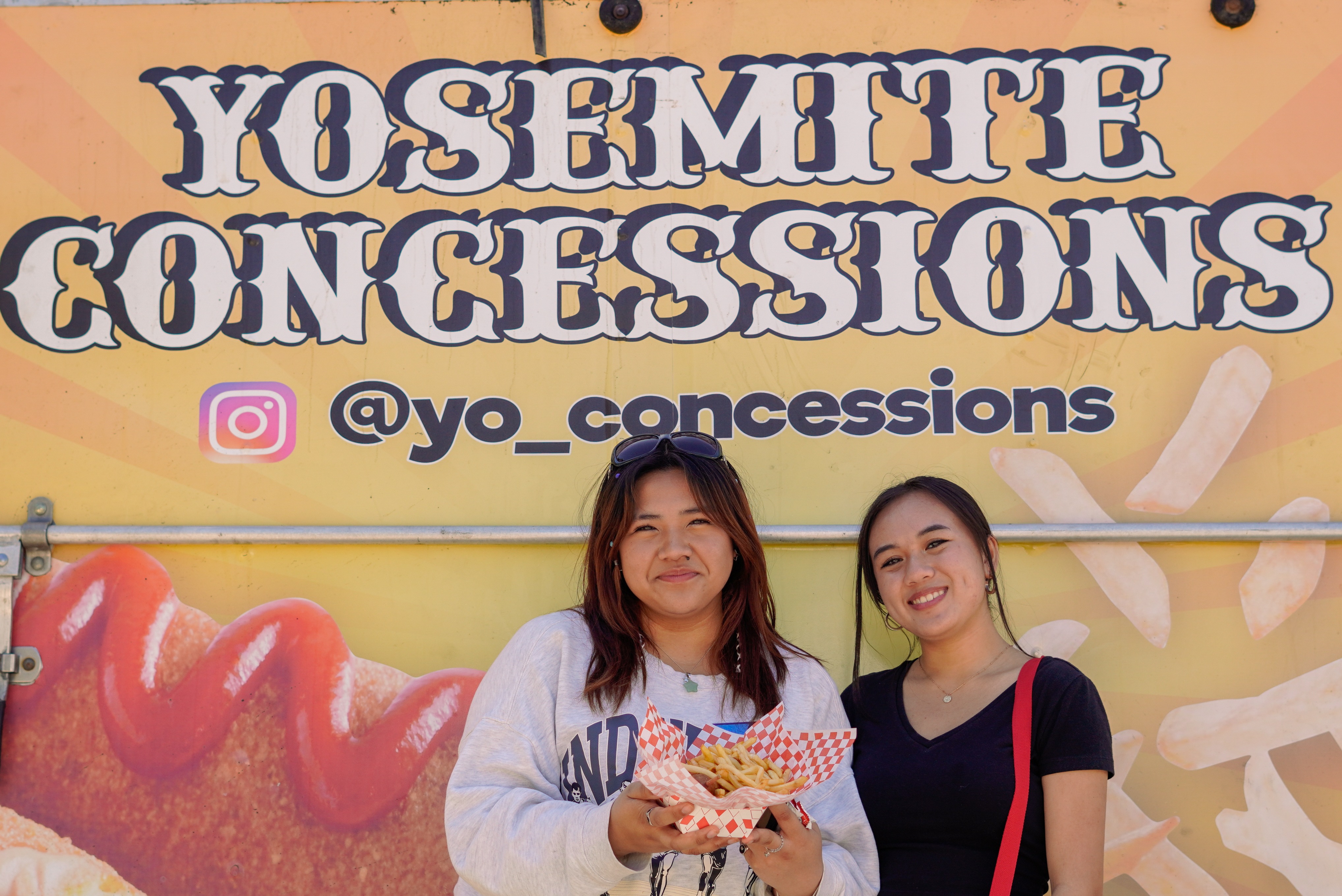 Two students pose in front of the Yosemite Concessions name and Instagram with their food